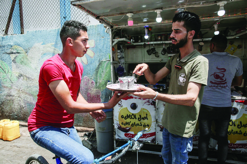 Shaaban Hamuda, 31,(R) a Palestinian business management graduate, gives instructions to one of his delivery employees carrying a tray of steaming cups of coffee, in front of his small stand near Rafah market, in the southern Gaza Strip, on July 13, 2020. - Hamuda's modest coffee on wheels business is giving the coastal Palestinian territory its first taste of a delivery service inspired by the likes of Uber Eats or Deliveroo. (Photo by SAID KHATIB / AFP)