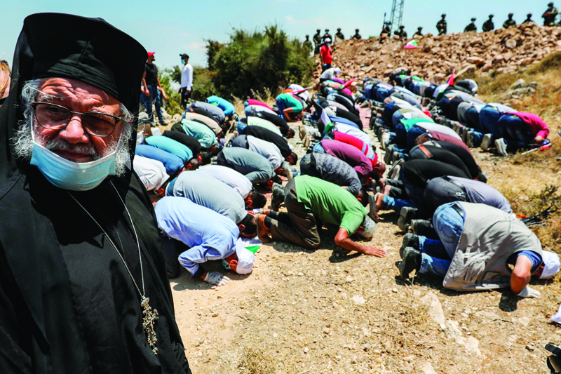 Archimandrite Abdullah Yulio (L), parish priest of the Melkite Greek Catholic church in Ramallah, stands by as Palestinians pray together during a protest against Jewish settlements and Israel's planned annexation of parts of the Israeli-occupied West Bank, in the town of Asira Shamaliya near the West Bank city of Nablus on July 10, 2020. (Photo by ABBAS MOMANI / AFP)