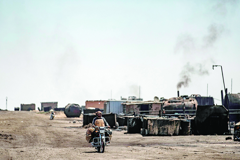AL QAHTANIYAH: A man drives a motorcycle past a makeshift refinery using burners to distill crude oil in the village of Bishiriya in the countryside near the town of Qahtaniya west of Rumaylan (Rmeilan) in Syria’s Kurdish-controlled northeastern Hasakeh province. —AFP