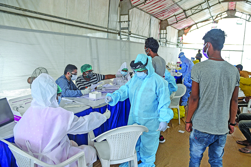 AHMEDABAD: Two health workers wearing Personal Protective Equipment (PPE) suits (left and center) collect a swab sample at a makeshift test point at Sanathal, on the outskirts of Ahmedabad on Friday. — AFP