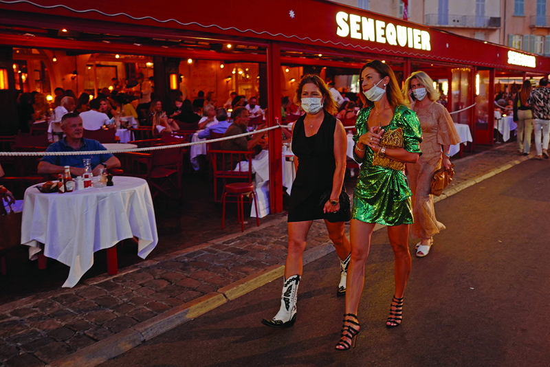 People wearing face masks walk past  'Le Cafe Senequier' situated along the Quai Jean Jaures,  on the Saint-Tropez harbour on August 8, 2020, as the city made wearing a protective mask mandatory in the town center. (Photo by Valery HACHE / AFP)