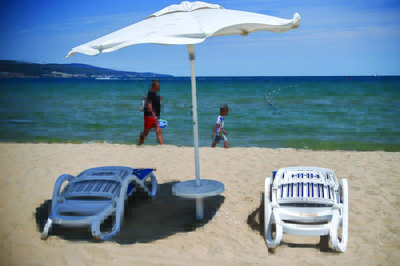 A photograph taken on July 16, 2020 shows tourists walking near empty sunbeds and umbrella in front of an hotel at the beach in Sunny Beach, Bulgaria's biggest Black Sea resort. - Bulgaria is the poorest country in the EU and will be dealt a body blow by the virtual collapse of its tourism sector, which accounts for 12 percent of annual economic output. Initially Bulgaria managed to control its infection numbers but after easing its lockdown comparatively early, it has found itself in the midst of a fresh spike in infections. (Photo by NIKOLAY DOYCHINOV / AFP)
