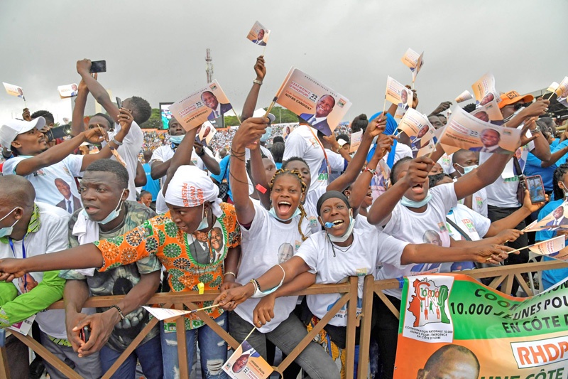 Supporters holding flags cheer as Ivory Coast's president Alassane Ouattara speaks at the Felix Houphouet-Boigny stadium on August 22, 2020 in Abidjan during his investiture by his ruling party as presidential candidate. - Ivory Coast President Alassane Ouattara was formally chosen by his ruling party on August 22 to run for a third term in an October election, despite furious opposition charges that the move is unconstitutional. (Photo by Issouf SANOGO / AFP)