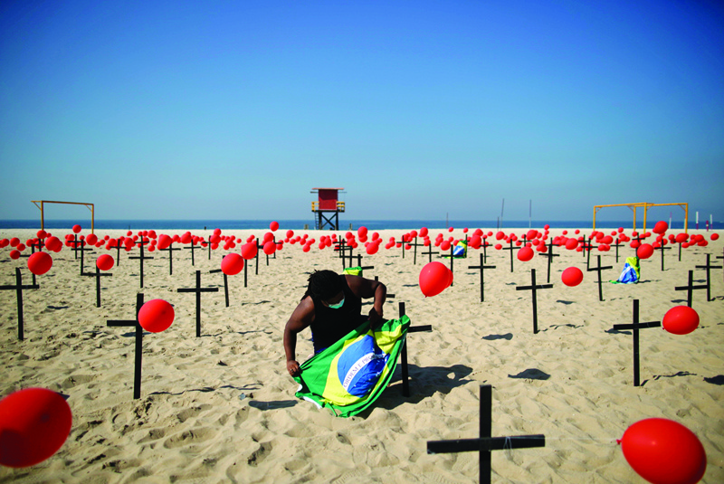 TOPSHOT - A demonstrator with a Brazilian flag is seen beside crosses during a tribute to COVID-19 victims organized by the Rio de Paz NGO at the Copacabana beach in Rio de Janeiro, Brazil, on August 08, 2020. (Photo by MAURO PIMENTEL / AFP)