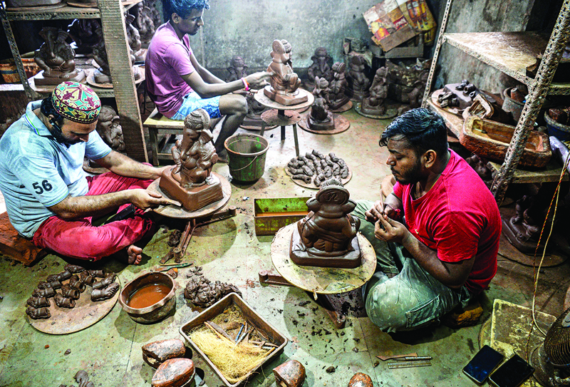In this picture taken on August 15, 2020, Muslim potter Yusuf Zakaria Galwani (L) along with his staff, work on the idols of elephant headed Hindu god Ganesha at his workshop at Kumbharwada inside the Dharavi slums in Mumbai. - After the coronavirus pandemic clobbered his pottery business, a Muslim artisan from India's largest slum turned to a Hindu god to revive his fortunes by making environmentally-friendly Ganesha idols for an upcoming festival. In Mumbai's Dharavi slum, Galwani worked alongside his two brothers to create 13-inch tall figurines out of terracotta clay, counting on the god -- who is revered as the remover of obstacles -- to give his business a much-needed boost. (Photo by INDRANIL MUKHERJEE / AFP)