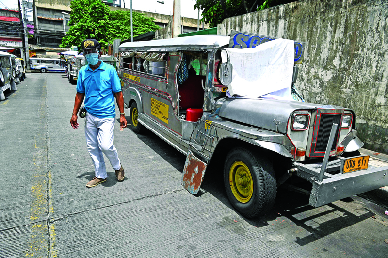In this photo taken on August 12, 2020, a resident walks past jeepneys serving as temporary homes parked along a road in Manila. - Jeepney drivers have not picked up passengers in Manila since March when the popular minibuses were forced off the road by a coronavirus lockdown that has left millions out of work. (Photo by Ted ALJIBE / AFP) / TO GO WITH AFP STORY: Health-virus-Philippines-transport, FOCUS by Ron LOPEZ