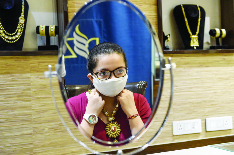 In this photograph taken on July 31, 2020, a customer wearing a facemask as a preventive measure against the COVID-19 coronavirus tries a necklace made of gold at jewellery shop 'DB Zaveri Pvt Ltd' in Ahmedabad. - As gold's value skyrockets, jewellers in India, traditionally one of the world's hottest markets, are struggling -- with shops shut, sales down and craftsmen staying home due to coronavirus fears. (Photo by SAM PANTHAKY / AFP) / TO GO WITH: NDIA-ECONOMY-GOLD-JEWELLERY-VIRUS by Ammu Kannampilly