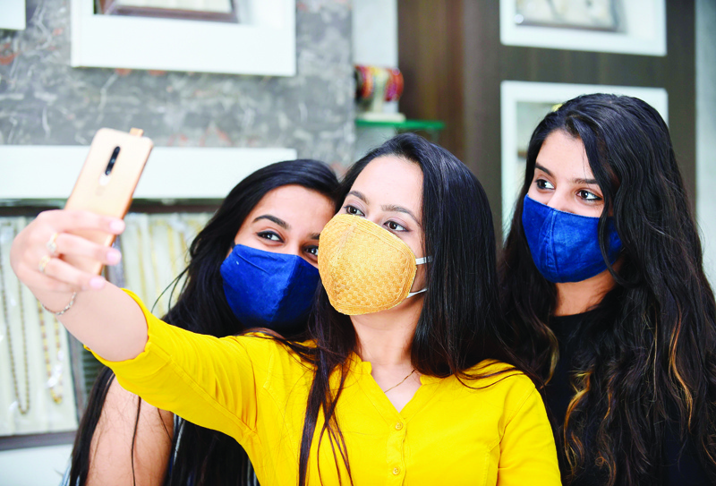 A customer (C) wearing a handmade facemask made with threads of gold takes selfie pictures with her friends at a jewellery shop in Chandkheda area in Ahmedabad on August 11, 2020. (Photo by SAM PANTHAKY / AFP)
