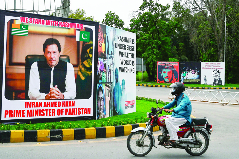 A motorcyclist rides past a billboard displaying a picture of Pakistan's Prime Minister Imran Khan along a street in Islamabad on August 4, 2020 ahead of the Yaum-i-Istehsal or Day of Exploitation on August 5, on the first anniversary after India scrapped Muslim-majority region Kashmir's semi-autonomous status and imposed a major security clampdown. (Photo by Aamir QURESHI / AFP)