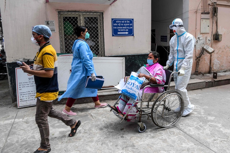 A medical staff wearing a Personal Protective Equipment (PPE) suit (R) shifts a patient in a wheelchair near a COVID-19 coronavirus ward at a hospital in New Delhi on August 12, 2020. (Photo by Prakash SINGH / AFP)