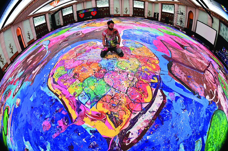 A picture taken with fisheye lens shows contemporary British artist Sacha Jafri sitting on his record-breaking painting entitled 'The Journey of Humanity' on September 23, 2020, as he speaks to people in the Emirati city of Dubai. - The painting, which measures the size of two football fields, can be seen at a hotel in Dubai, where Jafri spent months of lockdown due to the coronavirus pandemic. nThe gigantic artwork is part of his project 'Humanity Inspired' and with it he hopes to raise 30 million USD to fund health and education initiatives for children living in poverty worldwide. (Photo by GIUSEPPE CACACE / AFP)