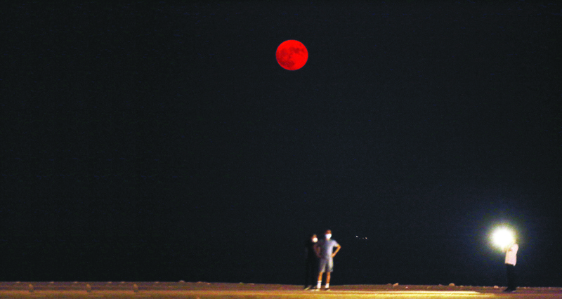 People walking on the beach as the Full Corn Moon rises in the sky over the Salmiya district, some 20 kilometres (12 miles) east of the capital Kuwait City on September 2, 2020.