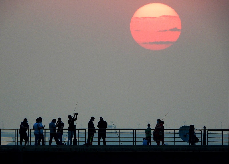 People walk along a boardwalk that stretches into the sea as the sun sets over the Kuwait capital Kuwait City on September 4, 2020. (Photo by YASSER AL-ZAYYAT / AFP)