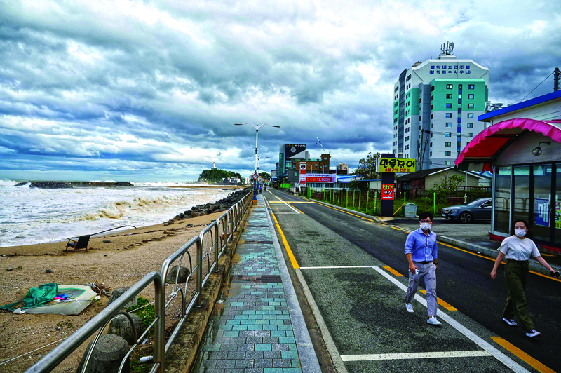 People walk along a coastal road watching the waves brought by Typhoon Haishen in the eastern port city of Sokcho on September 7, 2020. - The powerful typhoon lashed South Korea on September 7 after smashing into southern Japan with record winds and heavy rains that left four people missing in a landslide. (Photo by Ed JONES / AFP)