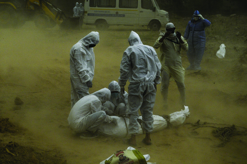 EDITORS NOTE: Graphic content / (FILES) In this file photo taken on May 10, 2020 Relatives wearing protective gear tie up the dead body of a victim who died from the COVID-19 coronavirus before the burial at a graveyard in New Delhi. - More than one million people have died from the coronavirus, according to an AFP toll, with no let-up in a pandemic that has ravaged the world economy, inflamed diplomatic tensions and upended lives from Indian slums and Brazilian jungles to America's biggest city. (Photo by SAJJAD HUSSAIN / AFP)