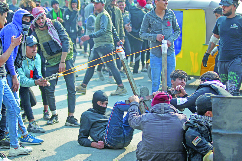 (FILES) In this file photo taken on January 30, 2020, Iraqi protesters use a slingshot to hurl rocks during clashes with security forces following a demonstration at Al Wathba square in the capital Baghdad. - In October 2019, unprecedented demonstrations across Iraq demanded the downfall of the ruling class. But after a year, a new government and nearly 600 protesters killed, virtually nothing has changed. (Photo by AHMAD AL-RUBAYE / AFP)