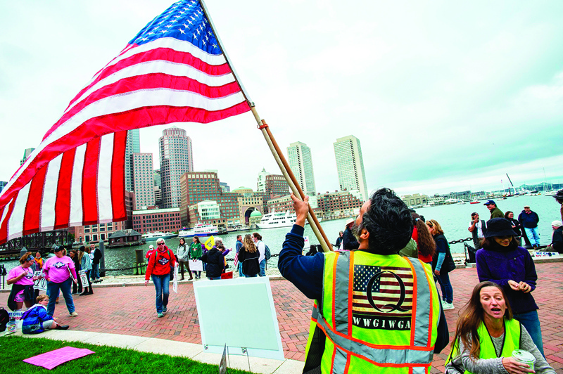 A man in a QAnon vest unfurls a US Flag as demonstrators gather to protest a mandatory flu vaccine order for children and to protest government mandates when it comes to medical choices outside the John Joseph Moakley United States Federal Courthouse in Boston, Massachusetts on October 5, 2020. (Photo by Joseph Prezioso / AFP)