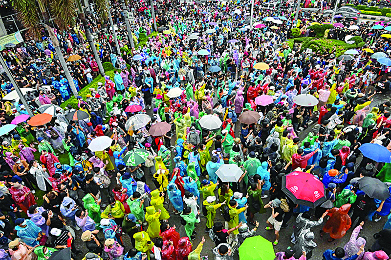 TOPSHOT - Pro-democracy protesters wear ponchos and use umbrellas to shelter from the rain at Wongwian Yai in Bangkok on October 17, 2020, as they continue to defy an emergency decree banning gatherings. (Photo by Mladen ANTONOV / AFP)