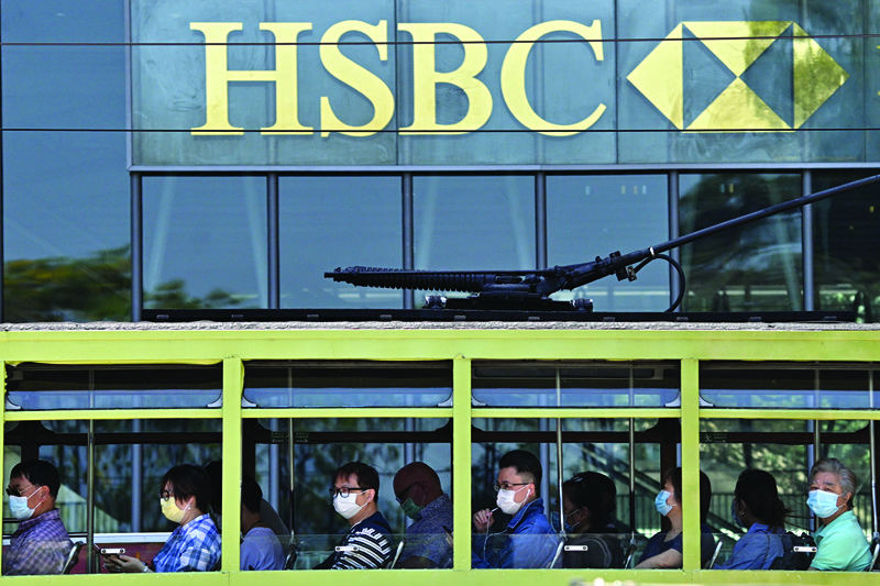 (FILES) In this file photo taken on April 28, 2020, commuters wearing face masks travel on a tram past HSBC signage displayed outside the bankís local headquarters in Hong Kong. - HSBC said on October 27, 2020 its third-quarter post-tax profits plunged 46 percent on-year as the Asia-focused banking giant continued to take a hammering from the coronavirus pandemic and spiralling China-US tensions. (Photo by Anthony WALLACE / AFP)