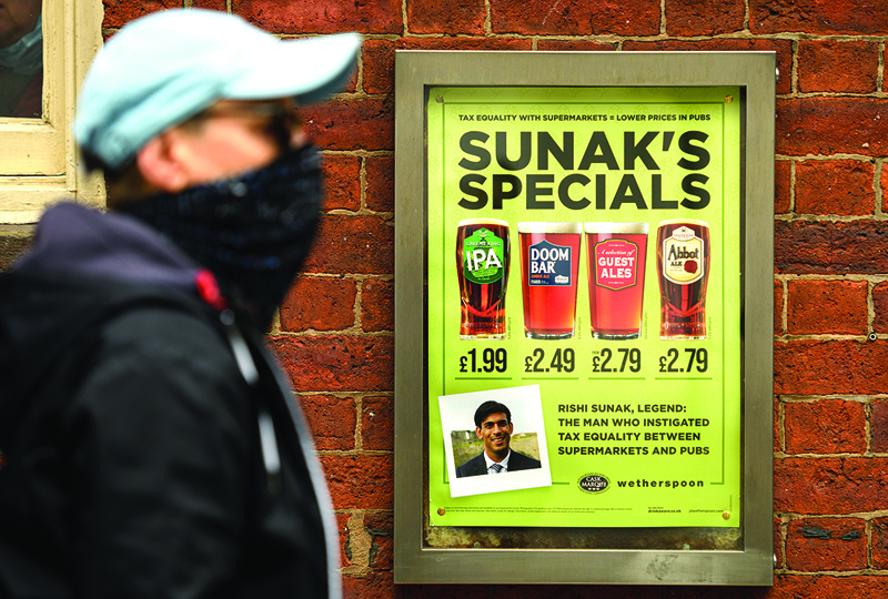 (FILES) In this file photo taken on August 30, 2020 a man walks past an advertisement for beers called 'Sunak's Specials', in reference to Britain's Chancellor of the Exchequer Rishi Sunak, outside of a pub in Manchester. - Pubs and restaurants in the UK are set to lose more than half a million jobs by the end of the year due to lower attendance, and shorter opening hours to counter the coronavirus pandemic, a survey conducted by trade association UKHospitality warned on October 6, 2020. (Photo by OLI SCARFF / AFP)