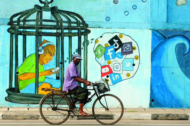 TOPSHOT - A man wearing a facemask as a preventative measure against the Covid-19 coronavirus rides a bicycle in front of a mural in Colombo on October 19, 2020. (Photo by LAKRUWAN WANNIARACHCHI / AFP)