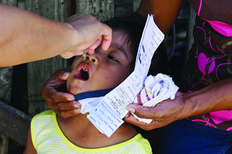 This photo taken on September 21, 2020 shows a municipal health worker (L) applying drops of a polio vaccine to child at a relocation site for informal settlers in San Jose Del Monte in Bulacan province, north of Manila. - Online misinformation is leaching out from cheap mobile phones and free Facebook plans used by millions of poor in the Philippines, convincing many to reject vaccinations for polio and other deadly diseases. (Photo by Ted ALJIBE / AFP) / TO GO WITH Health-virus-misinformation-internet-vaccine-Philippines,FOCUS by Jake Soriano