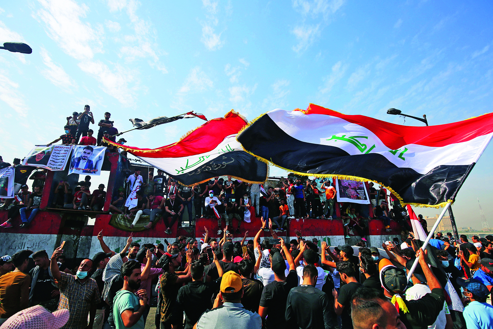 TOPSHOT - Iraqi demonstrators wave flags as they gather in Tahrir Square in the centre of the capital Baghdad on October 25, 2020, to mark the first anniversary of a massive anti-government movement demanding the ouster of the entire ruling class accused of corruption. - Thousands of Iraqis headed to the capital Baghdad's iconic Tahrir Square and the Green Zone, where authorities sit, to mark the first anniversary of an ongoing revolt against the country's stagnant political class. (Photo by AHMAD AL-RUBAYE / AFP)