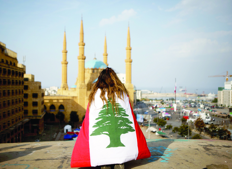 (FILES) In this file photo taken on November 14, 2019, a Lebanese anti-government protester, draped in a national flag, sits on the rooftop of 'The Egg' buidling overlooking the Mohammed al-Amin mosque and the Martyrs square in the capital Beirut's downtown district. - Lebanon is now suffering though one of the darkest periods in its chaotic history, and soaring poverty combined with a seemingly inexorable brain drain make for a bleaker future yet. (Photo by Patrick BAZ / AFP)