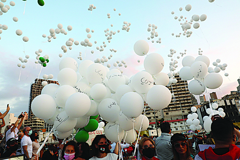 TOPSHOT - People gather to release white balloons near the seaport of Beirut on October 4, 2020, to commemorate the second month after the August 4 massive explosion there that killed at least 190, injured more than 6500 and ravaged entire neighbourhoods of the Lebanese capital leaving scores of residents homeless. - Dozens of demonstrators gathered near what remains of Beirut's port today to mark two months since a huge explosion widely blamed on Lebanon's political class.nTwo months later, an investigation into the disaster has yet to make public its results, further stoking public anger in a country mired in economic crisis and battered by the coronavirus pandemic. (Photo by ANWAR AMRO / AFP)