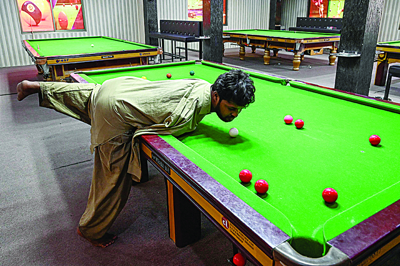 In this picture taken on September 28, 2020, Muhammad Ikram plays a shot with his chin at a local snooker club in Samundri. - Ikram, who was born without arms, steps up to a snooker table, sizes up his options and with a firm flick of his chin strikes the cue ball and slots a red into a corner pocket. The sport was perhaps an unlikely passion for Ikram, 32, to pursue, but the Pakistani player has spent years honing his skills and can now give anyone at his local snooker hall a run for their money. (Photo by Aamir QURESHI / AFP) / TO GO WITH 'Pakistsan-disabled-society-snooker, FOCUS' by Zain Zaman Janjua