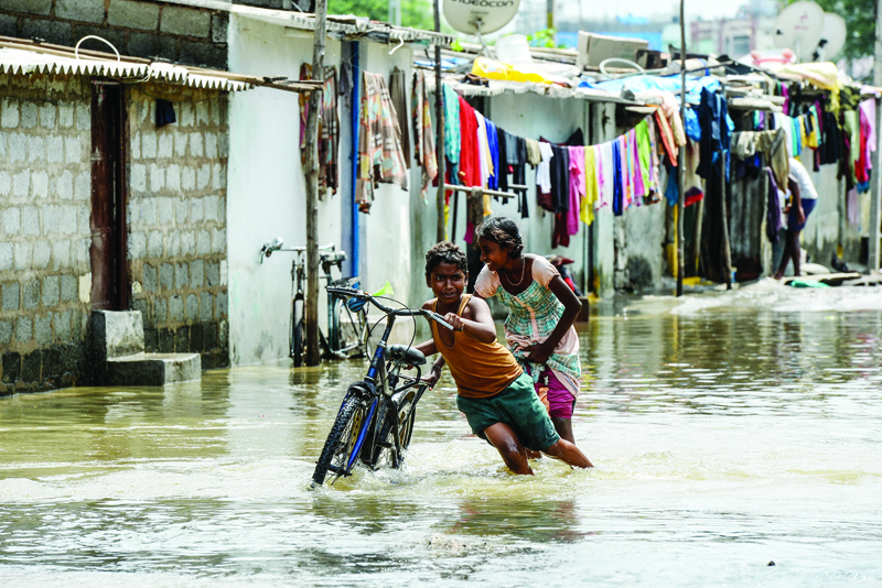 Children push a bicycle making their way on a flooded street following heavy rains in Hyderabad on October 15, 2020. (Photo by NOAH SEELAM / AFP)
