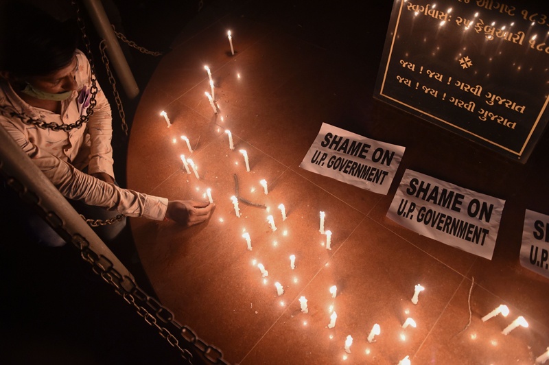 TOPSHOT - A member of the National Students' Union of India (NSUI) places a candle besides placards after a candlelight vigil following accusations of Indian Police forcibly cremating the body of a 19-year-old woman victim, who was allegedly gang-raped by four men in Bool Garhi village of Uttar Pradesh state, in Ahmedabad on September 30, 2020. - Indian police were accused on September 30 of forcibly cremating the body of a 19-year-old alleged gang-rape victim as anger grew over the latest horrific sexual assault to rock the country. The teenager from India's marginalised Dalit community suffered serious injuries in a brutal sexual attack two weeks ago, according to her family and police, and died at a New Delhi hospital on September 29. (Photo by SAM PANTHAKY / AFP)