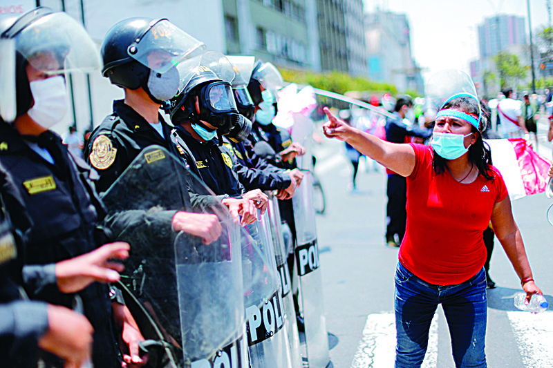 TOPSHOT - A woman gestures in front of police officers standing guard as people celebrate outside the Congress in Lima after Peruvian interim president Manuel Merino presented his resignation on November 15, 2020. - Peru's President Manuel Merino resigned Sunday, just five days after taking office, sparking celebrations in the capital Lima following street protests against him and the ousting of his popular predecessor. (Photo by Luka GONZALES / AFP)