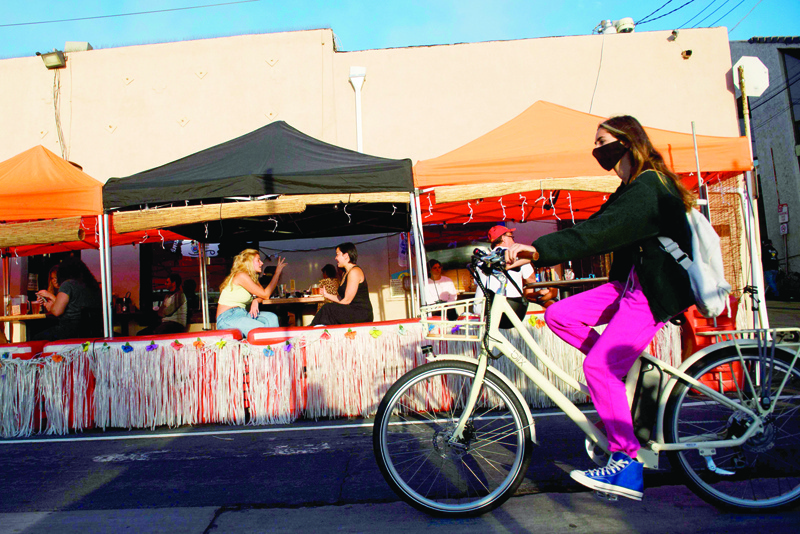 A cyclist wearing a face mask rides past outdoor diners in Manhattan Beach, California, November 21, 2020 a few hours before the start of the new 10:00 pm to 5:00 am curfew during increased Covid-19 restrictions. - The United States surpassed 12 million Covid-19 cases today, according to the Johns Hopkins University real-time tracker. (Photo by Patrick T. Fallon / AFP)
