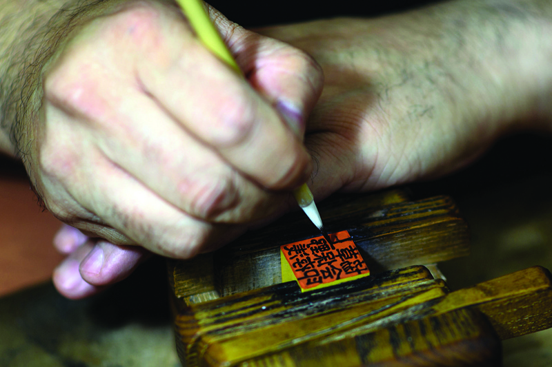 This picture taken on October 9, 2020 shows traditional ink stamp-maker Takahiro Makino, 44, writing characters on a hanko at a studio in Tokyo. - Hanko or traditional ink stamps are used to sign everything from delivery receipts to marriage certificates in Japan, and a push to digitise the nation and phase them out faces an uphill struggle. (Photo by Philip FONG / AFP) / TO GO WITH AFP STORY JAPAN-CULTURE-CRAFTS-ECONOMY-INTERNET-GOVERNMENT,FOCUS BY HARUMI OZAWA