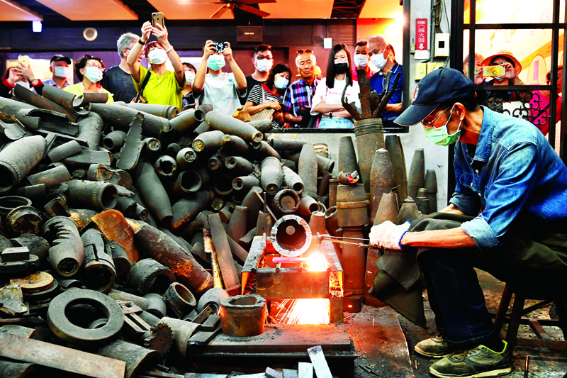 This photo taken on October 21, 2020 shows Taiwanese blacksmith Wu Tseng-dong (R), owner of a knife factory, giving a demonstration to tourists how to make a knife from cases of Chinese artillery shells which were fired decades ago from Xiamen on the mainland at Taiwan's Kinmen island - which lies off the coast of the Chinese mainland. - In a contemporary twist on beating swords into ploughshares, Taiwanese blacksmith Wu Tseng-dong has forged a career converting Chinese artillery shells once fired in anger into kitchen knives. (Photo by Sam Yeh / AFP) / TO GO WITH Taiwan-China-US-politics-military-Kinmen,SCENE by Amber WANG