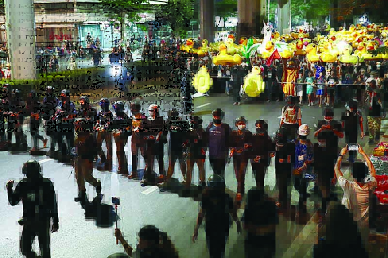 A line of pro-democracy protesters wearing helmets link hands as they walk in front of others carrying large inflatable ducks during a march to the 11th Infantry Regiment as part of an anti-government rally in Bangkok on November 29, 2020. (Photo by Jack TAYLOR / AFP)