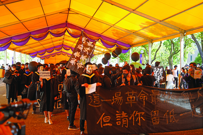 Students from the Chinese University of Hong Kong (CUHK), wearing graduation gowns and and masks, display slogans that authorities say are now illegal under a new security law, at a protest in memory of the pro-democracy demonstrations at CUHK a year ago during graduation festivities at the campus in the Shatin area of Hong Kong on November 19, 2020. (Photo by Yan ZHAO / AFP)