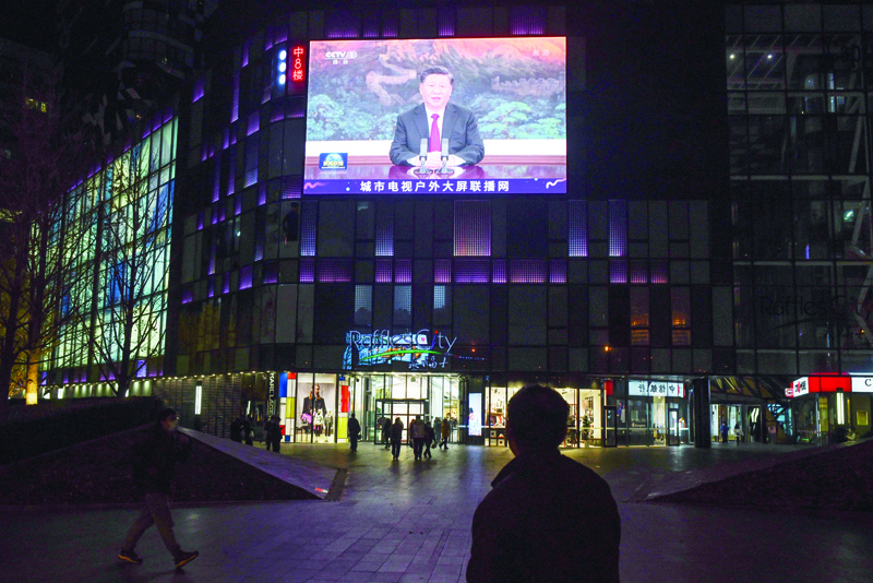 People walk below a giant screen showing news coverage of China's President Xi Jinping's speech via a virtual meeting to the Asia-Pacific Economic Cooperation (APEC) forum in Malaysia, outside a shopping mall in Beijing on November 19, 2020. (Photo by GREG BAKER / AFP)