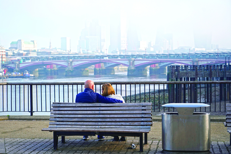 A couple sit on a bench as the fog lifts over the skyline of the City of London on November 5, 2020, as England enters a second novel coronavirus COVID-19 lockdown. - England's 56 million people joined much of western Europe in a second coronavirus lockdown Thursday, as the United States set a fresh daily record with close to 100,000 new infections. (Photo by Niklas HALLE'N / AFP)