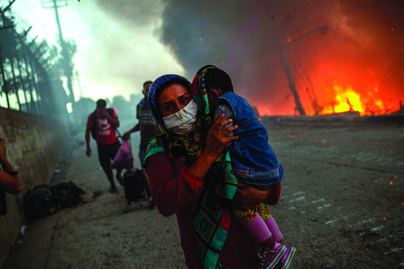 -- AFP PICTURES OF THE YEAR 2020 --nnA woman carries a child past flames after a major fire broke out in the Moria migrants camp on the Greek Aegean island of Lesbos, on September 9, 2020. - Thousands of asylum seekers were left homeless on on September 9 after a fire gutted Greece's largest migrant camp on Lesbos, plunging the island into crisis and provoking an outpouring of sympathy from around Europe and calls for reform of the refugee system. The blaze, which began hours after 35 people tested positive for coronavirus at the Moria camp, sent thousands fleeing for safety into surrounding olive groves -- but nobody was seriously hurt. (Photo by ANGELOS TZORTZINIS / AFP)