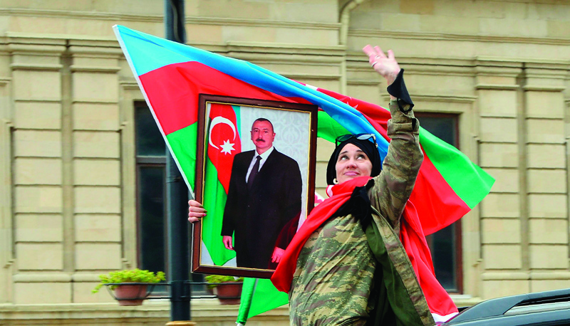 A woman holds the national flag and a portrait of  Azerbaijan's President Ilham Aliyev as people celebrate in the streets of the capital Baku on November 10, 2020, after Armenia and Azerbaijan agreed a ceasefire following a string of Azeri victories in fighting over the disputed Nagorno-Karabakh region. - Armenia and Azerbaijan agreed on a deal with Russia to end weeks of fierce clashes over Nagorno-Karabakh on November 10, 2020, after a string of Azerbaijani victories in its fight to retake the disputed region. (Photo by Tofik BABAYEV / AFP)