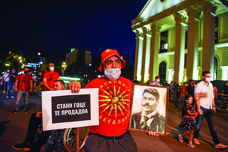 This photograph taken on September 15, 2020, shows a protestor wearing a T-shirt with an image  of the former Macedonian flag, holding a photograph of revolutionary figure Goce Delchev and a placard that reads 'Get up Goce, they sold you', as he takes part in an anti-government protest in Skopje. - After changing its name last year to settle a decades-old battle with Greece, the small Balkan state of North Macedonia was finally on a path to join the European Union. Until Bulgaria stepped in. (Photo by Robert ATANASOVSKI / AFP)