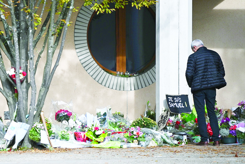 (FILES) In this file photo taken on October 19, 2020 A man looks at flowers layed outside the Bois d'Aulne secondary school in homage to slain history teacher Samuel Paty, who was beheaded by an attacker for showing pupils cartoons of the Prophet Mohammed in his civics class, in Conflans-Sainte-Honorine, northwest of Paris. - Four teenage students have been charged in France over the killing of Samuel Paty, a judical source said Thursday, including three for allegedly pointing out the teacher to his murderer. Three other pupils were charged earlier this month with complicity over the beheading last month of Paty, who had shown his students cartoons of the Prophet Mohammed as part of a lesson on free speech. (Photo by Anne-Christine POUJOULAT / AFP)