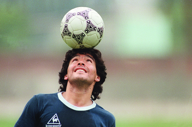 (FILES) In this file photo taken on May 22, 1986 Argentine football star Diego Maradona, wearing a diamond earring, balances a soccer ball on his head as he walks off the practice field following the national selection's practice session in Mexico City. - Argentinian football legend Diego Maradona passed away on November 25, 2020. (Photo by JORGE DURAN / AFP)