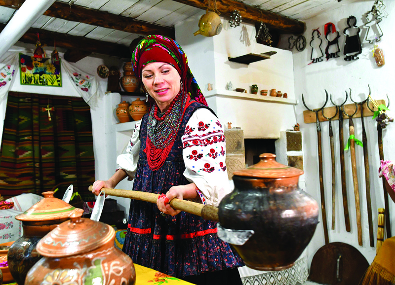 Olena Shcherban, Ukrainian ethnologist and historian, who studies borscht and has 365 of its unique recipes from all over Ukraine in her private collection, wearing Ukraine's traditional clothes and headdress cooks borscht in clay, pots in the wood stove in the village of Opishnya in Poltava region on November 26, 2020. - It was the beginning of October, when Ukraine announced its plan to have borscht, a dish usually made with beetroot and carrots widely recognised as part of its intangible cultural heritage. Kiev said it will submit an application to the United Nations cultural body UNESCO to set the record straight, and suddenly Russia got angry. (Photo by Genya SAVILOV / AFP)