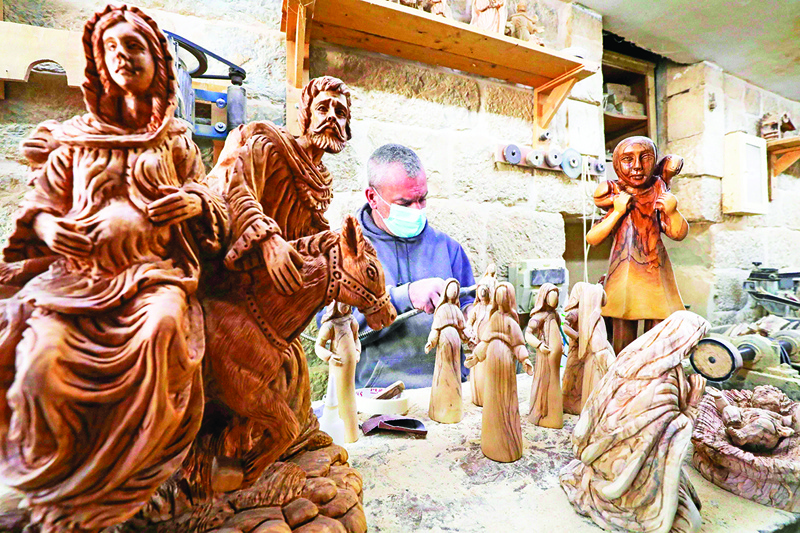 TOPSHOT - A Palestinian carpenter carves religious statues and figurines from olive wood at a shop near the Church of the Nativity, in the West Bank city of Bethlehem on December 21, 2020. (Photo by HAZEM BADER / AFP)