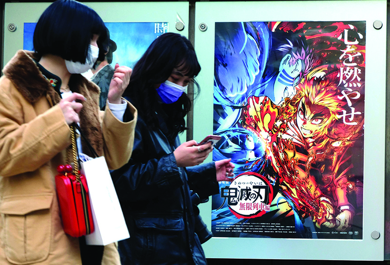 In this picture taken on December 16, 2020, pedestrians walk past a poster promoting the anime movie Demon Slayer -- Kimetsu no Yaiba the Movie: Mugen Train -- at a cinema in Tokyo. - An anime epic in which a teenager hunts down and beheads demons has become the surprise sensation of Japanese cinema during the pandemic, and could soon be the country's top-grossing film of all time. (Photo by Kazuhiro NOGI / AFP) / To go with AFP story  Japan-entertainment-film-anime-health-virus, FOCUS by Mathias CENA, Katie Forster