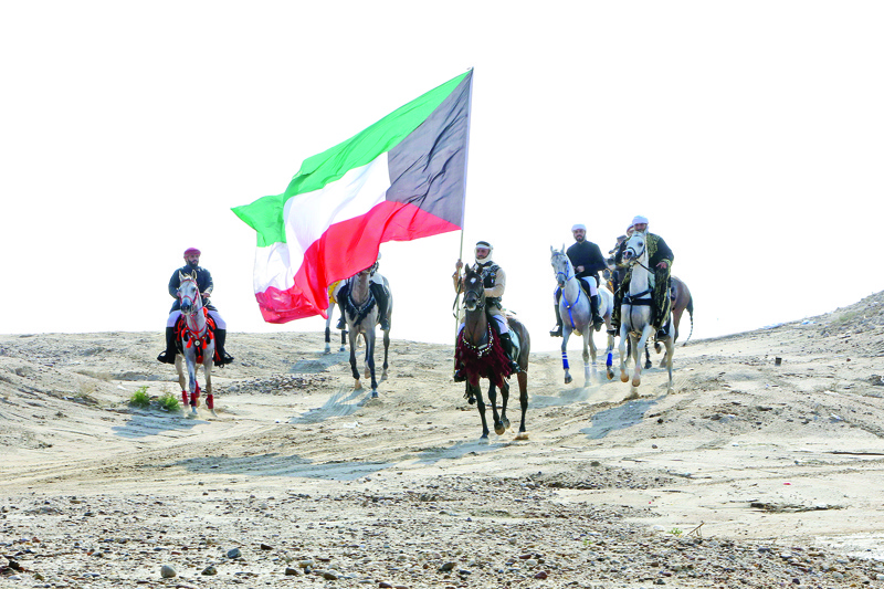 Members of the Kuwaiti knights team carry a national flag as they perform with their horses on the sea side, 70 kms west of the capital Kuwait City on December 11, 2020. (Photo by YASSER AL-ZAYYAT / AFP)