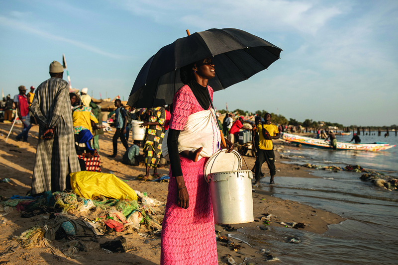 A woman carrying a baby in a sling onher back waits to buy fresh fish at the fishing port in Mbour on November 16, 2020. - Mbour has in the recent months been a popular departure site for illegal migrants wanting to reach Europe. Lack of work for youth and the dwindling fish stocks is driving young Senegalese fishermen to find opportunity elsewhere. In the last two weeks of October 2020 alone, four hundred and eighty migrants where registered dead or missing along the coast of Senegal whilst trying to illegally make the crossing to the Canary Islands. (Photo by JOHN WESSELS / AFP)